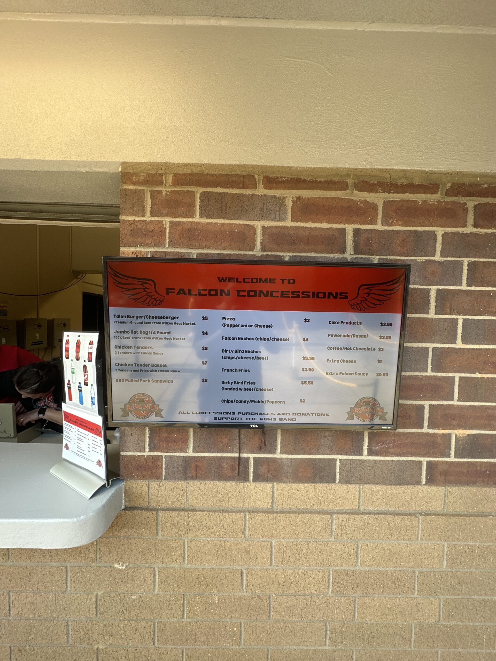Concession stand monitor displaying the menu.A volunteer is in the background going through a cash box.